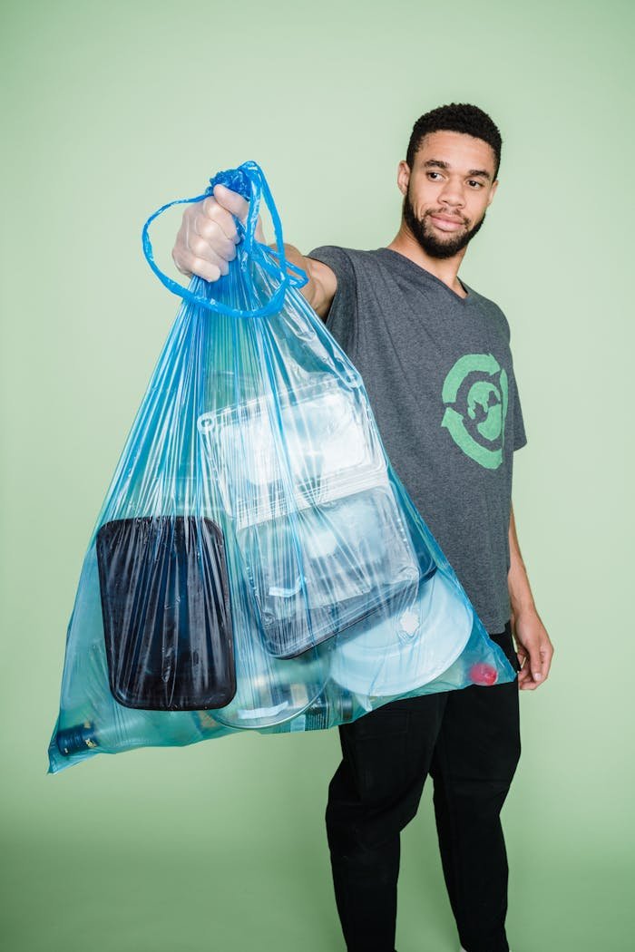 Young man holding a bag of plastic waste, promoting environmental conservation. Studio setting, green background.